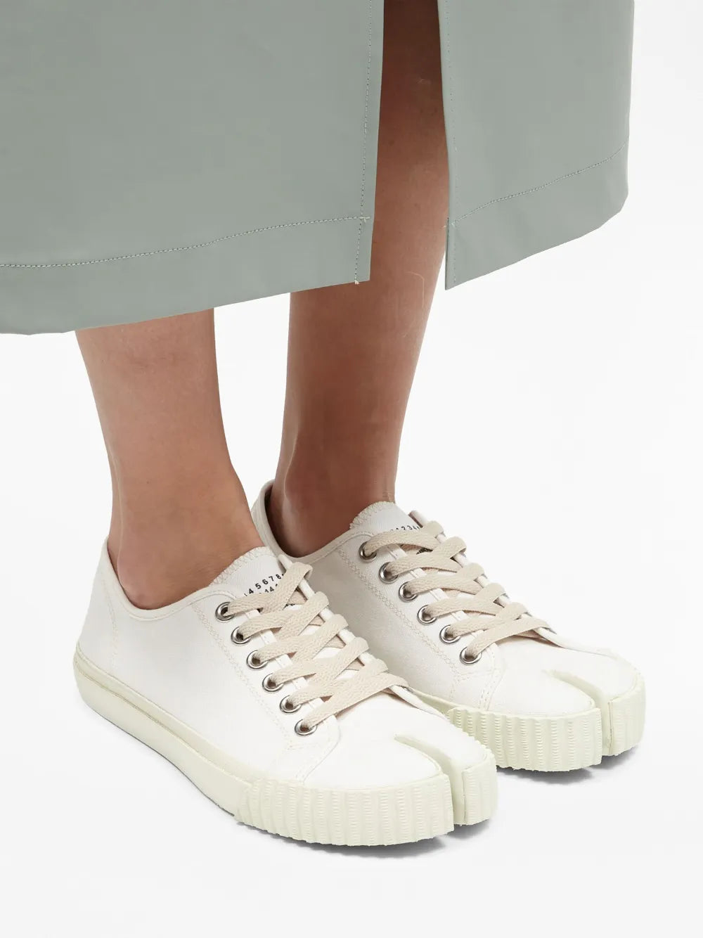 White Tabi low-top sneakers on feet, lace-up closure and thick textured sole.