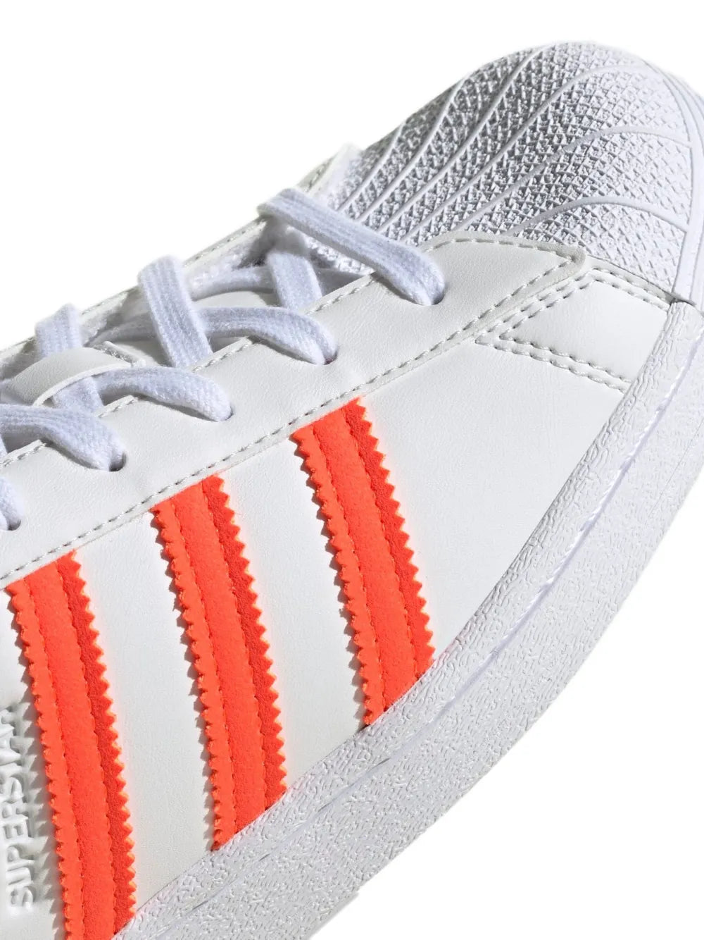 adidas Superstar close-up: white leather upper with orange triple stripes and lace