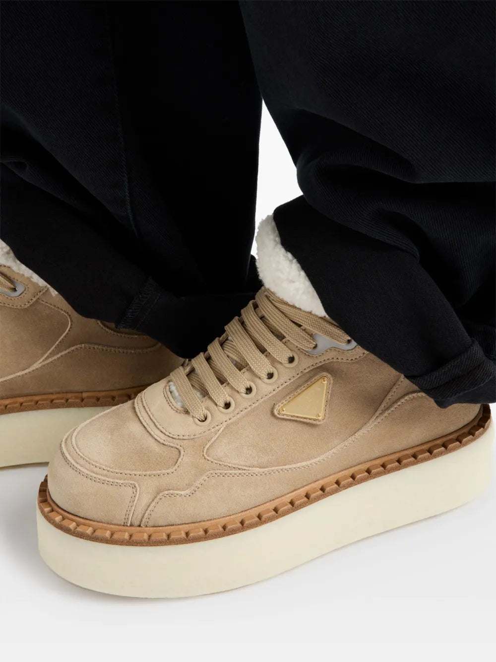 Suede sneakers with shearling trim and triangular logo patch, worn with dark pants
