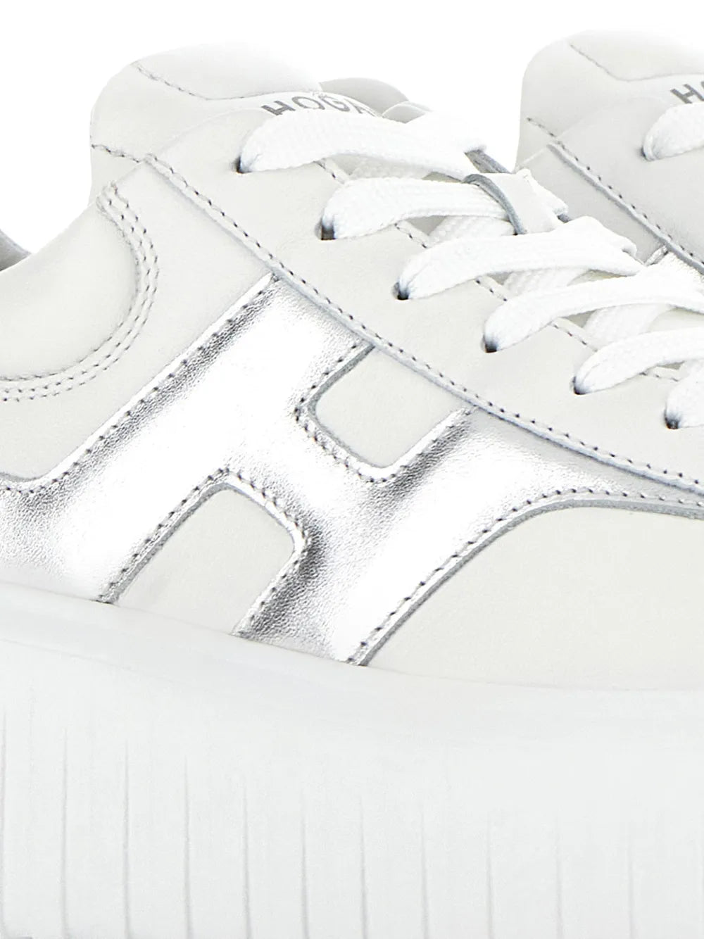White Hogan H-Stripe sneakers close-up: stitched leather, silver H-panel, lace eyelets.