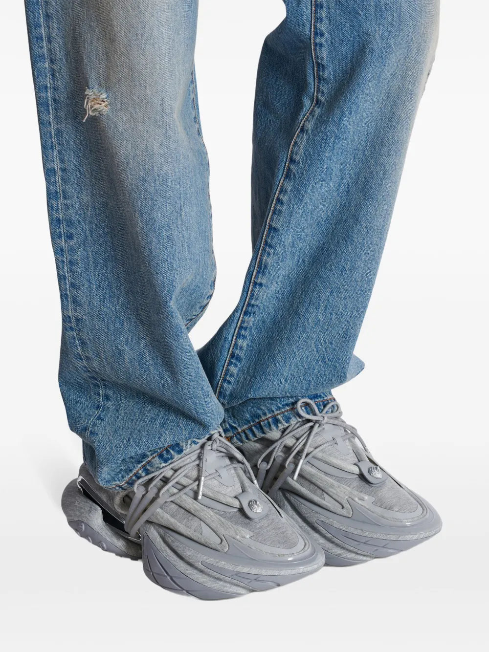 Medium grey sneakers worn with light-wash jeans, lace-up style with chunky rubber soles
