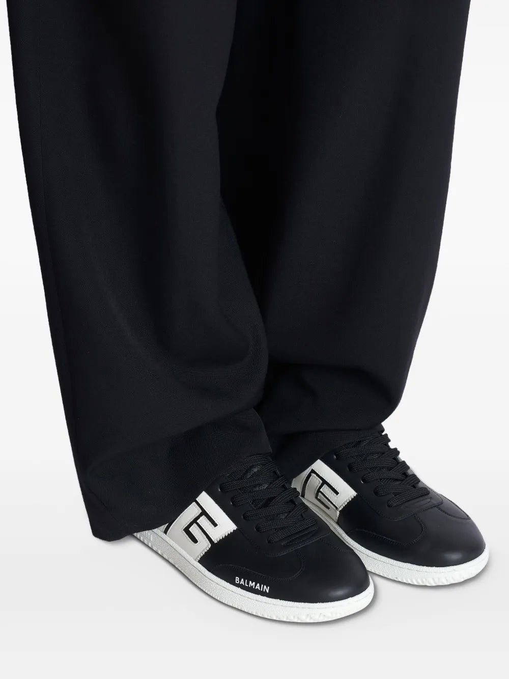 Black sneakers on feet with white sole and white Balmain B emblem