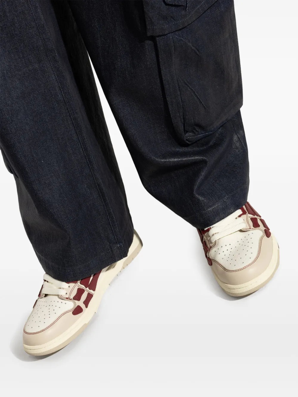 White and red lace-up sneakers with perforated toe, worn with dark jeans