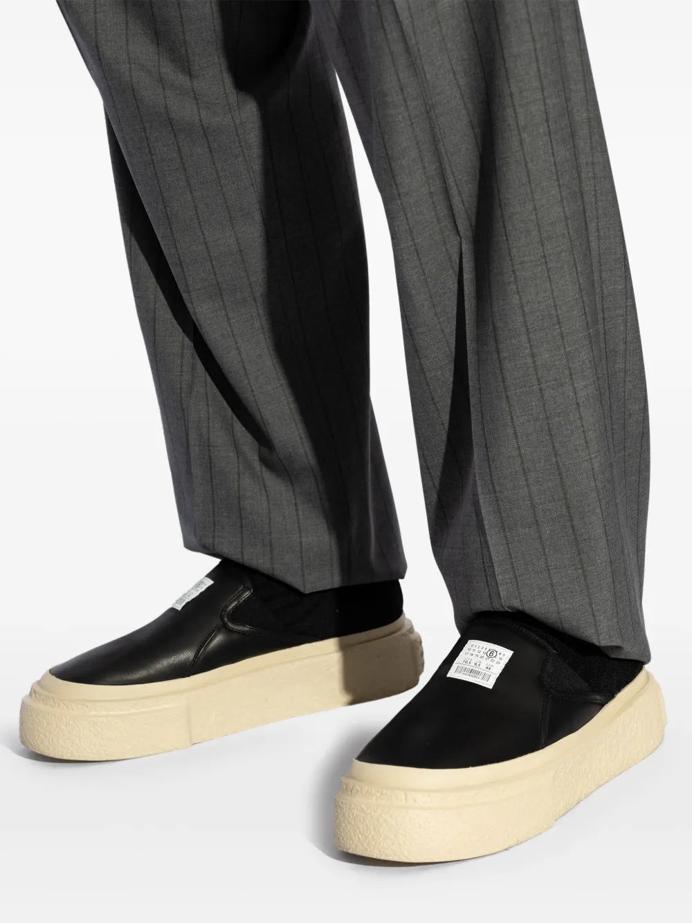 Black sock-insert sneakers with beige platform sole, shown with gray trousers