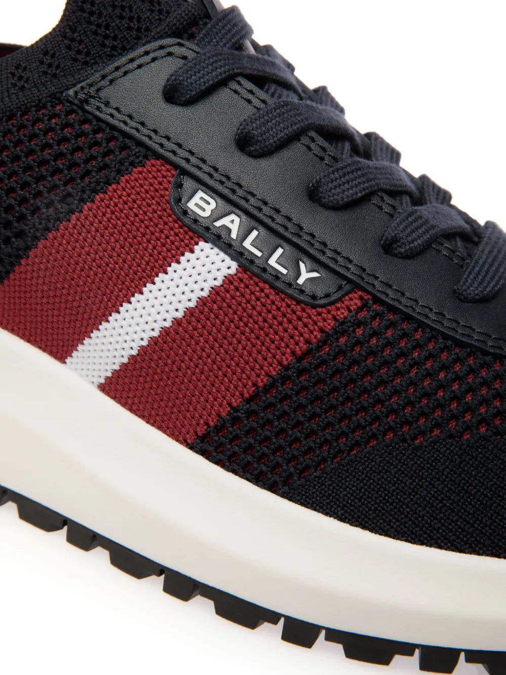 Bally Darnell-T sneaker close-up: dark knit, red/white stripe, rubber sole tread.