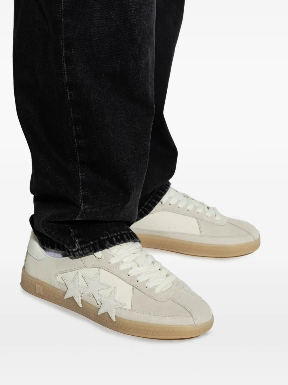 Light grey low-top sneakers on feet with three white star patches and gum sole