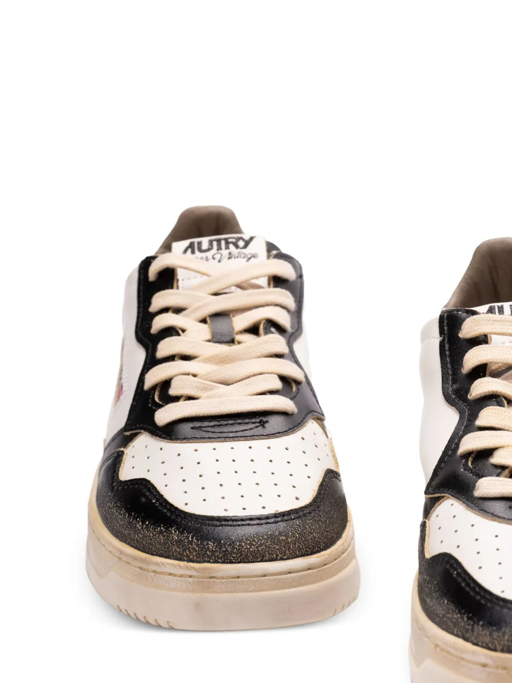 Close-up of lace-up sneakers with white perforated toe, black panels, and Autry logo.
