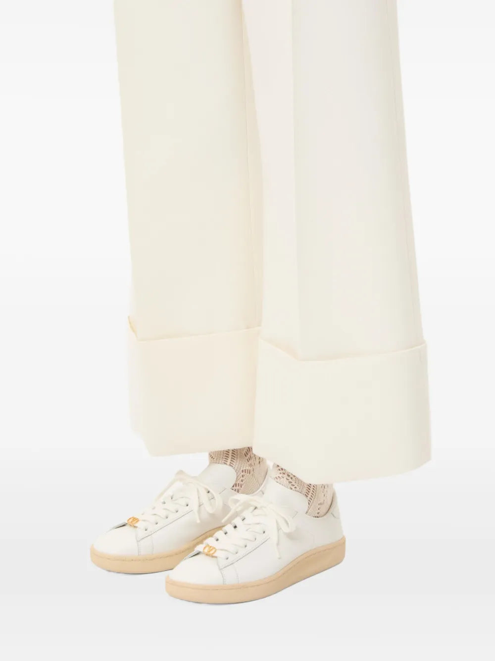 White low-top sneakers with tan sole worn with light trousers