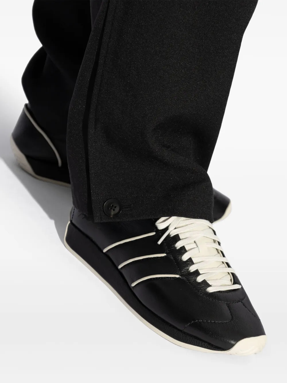 Close-up of black sneaker with white three stripes, cream laces, and dark sole