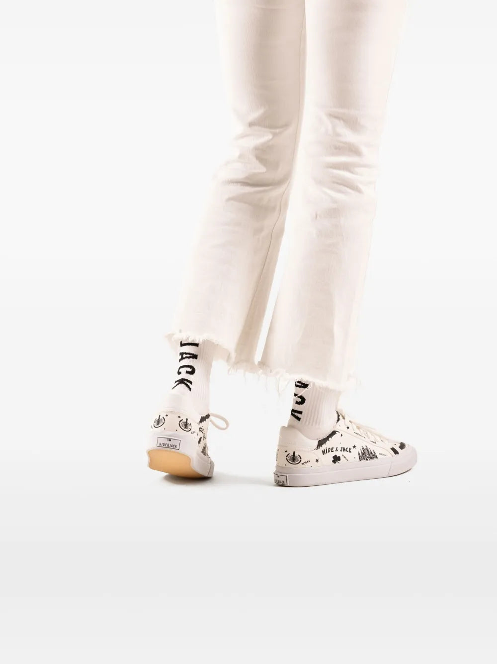 Hide&Jack Toby white sneakers with black graphic print, worn with white jeans.