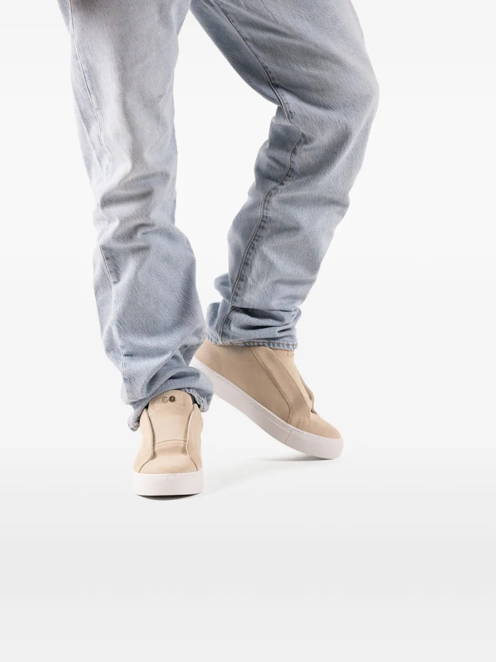Beige suede slip-on sneakers with low-profile white sole, worn with jeans.