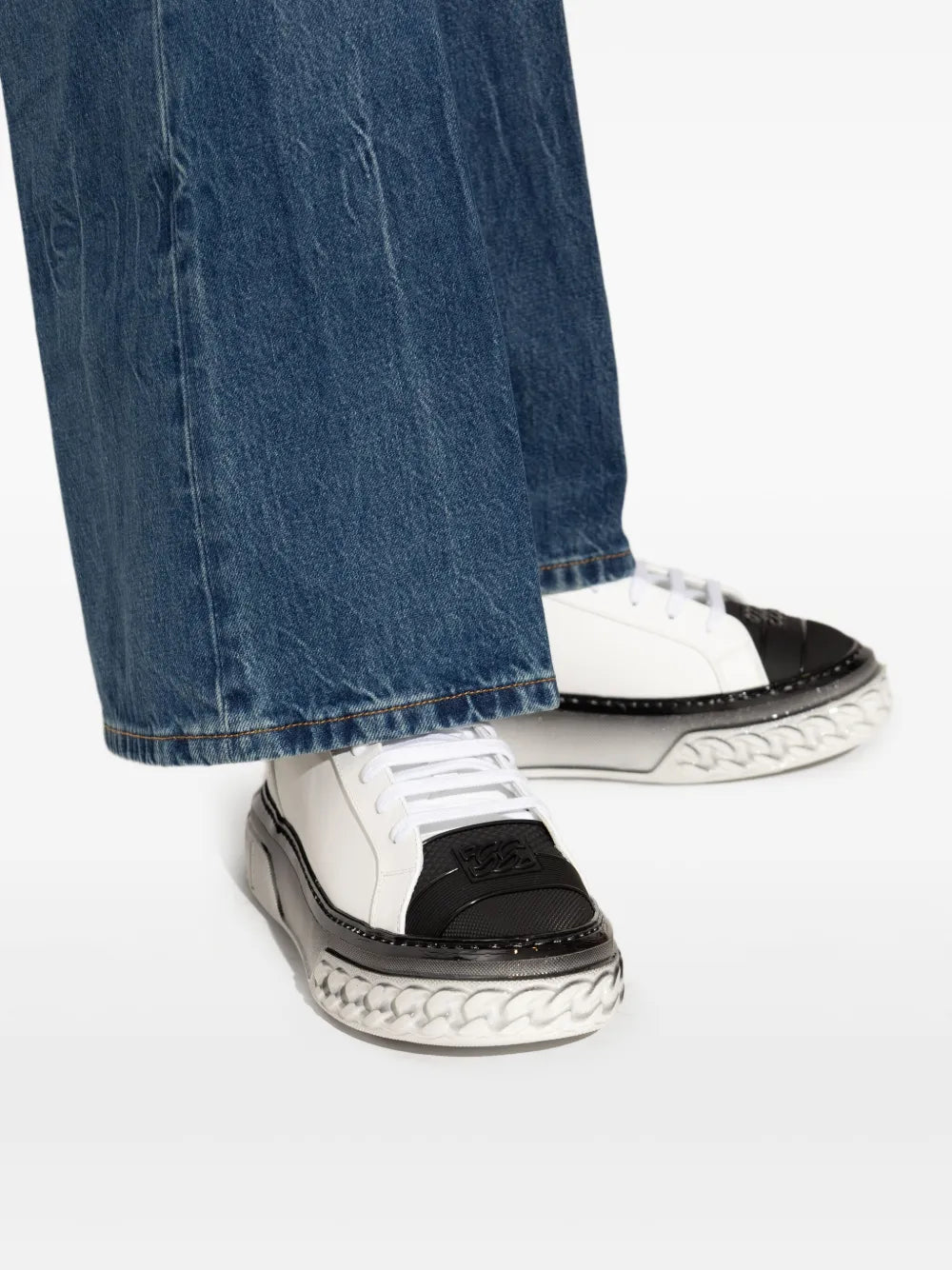 Close-up of white and black lace-up sneakers with chunky sole under jeans hem.
