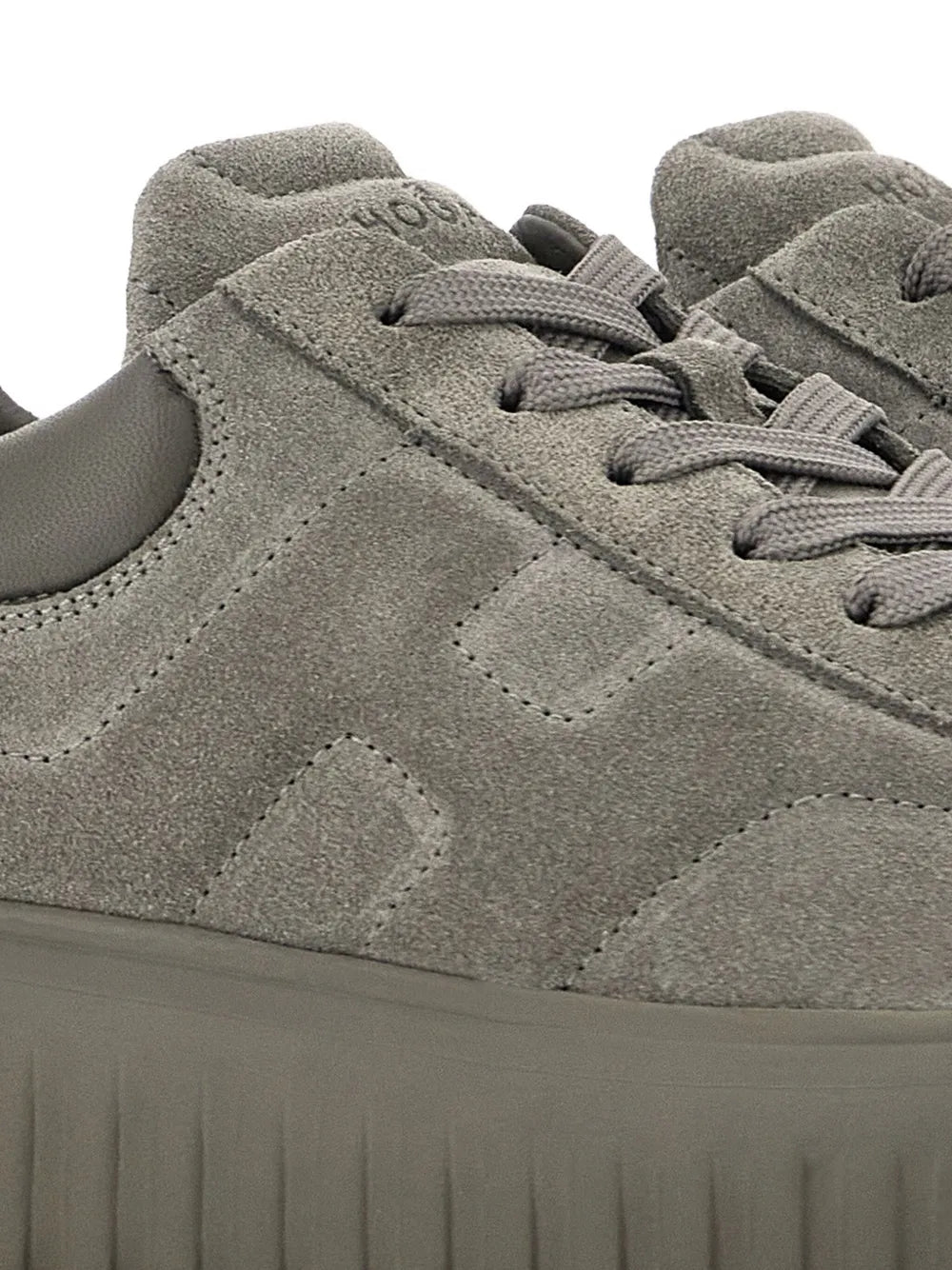 Grey suede sneaker upper close-up with lace eyelets, seam details, and rubber sole