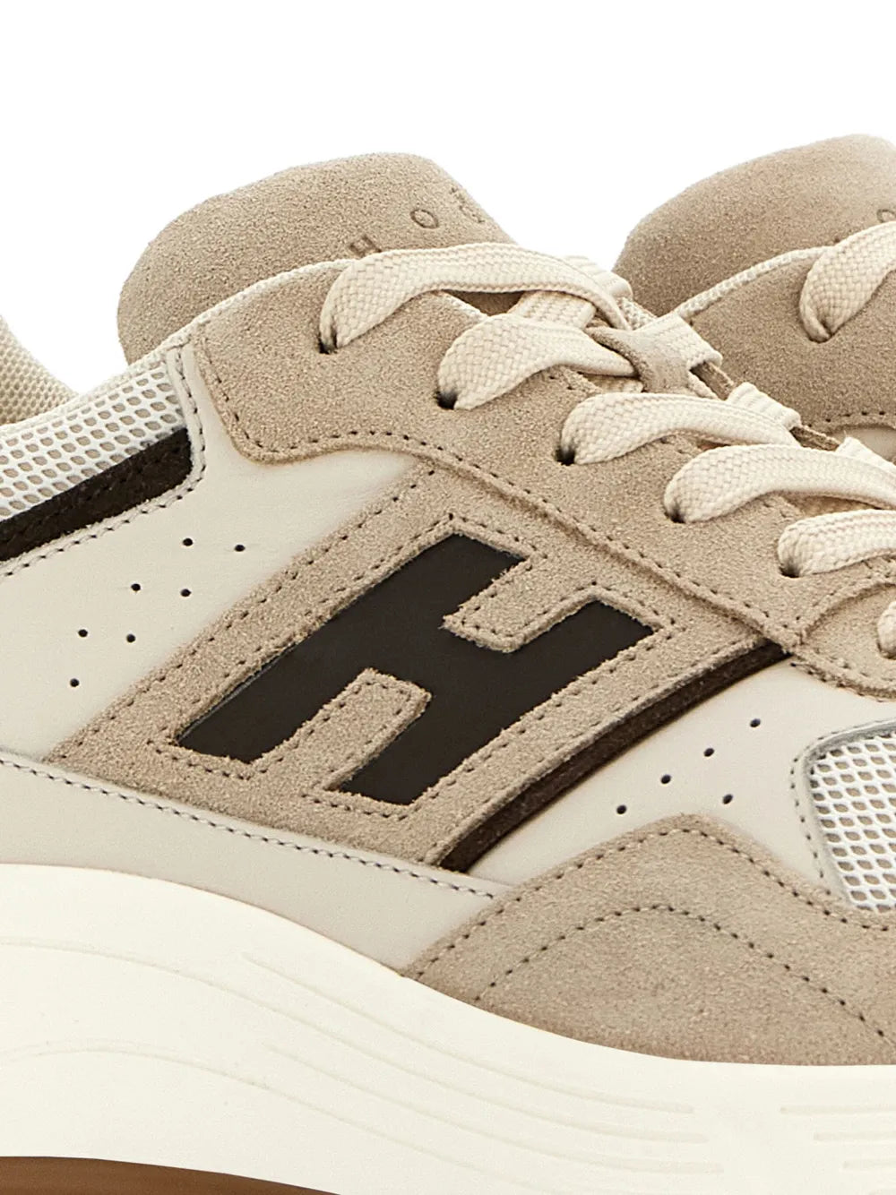 Close-up of light beige sneaker upper with suede panels, laces, and black H logo