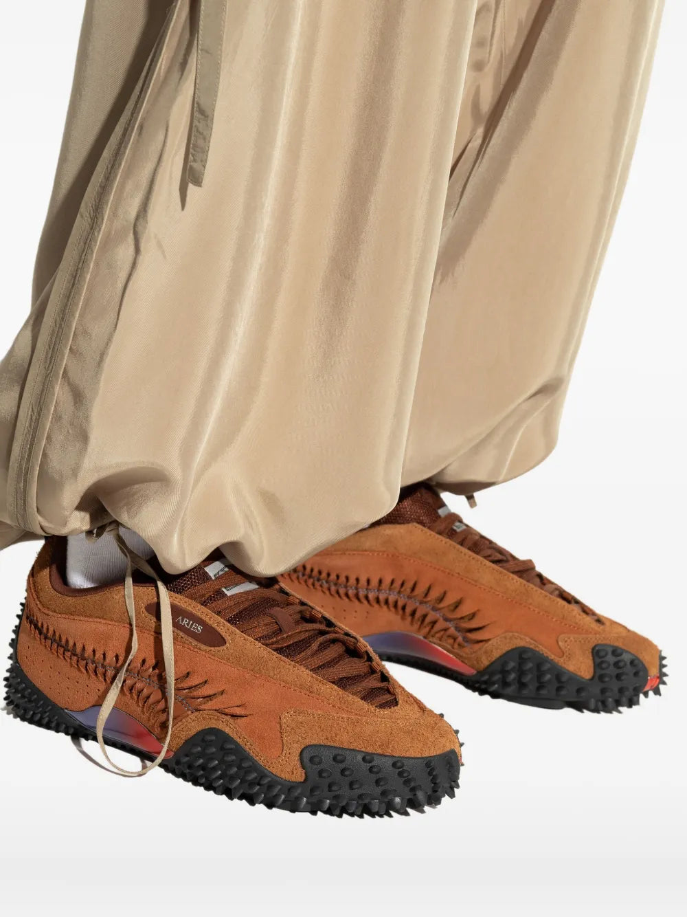 Pair of brown low-top sneakers with black studded soles and red under-arch panel