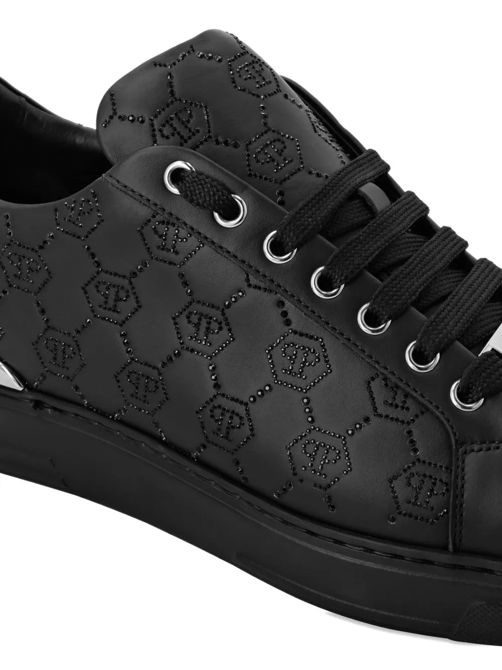 Black logo-embellished sneaker upper close-up with laces, eyelets, and embossed motif