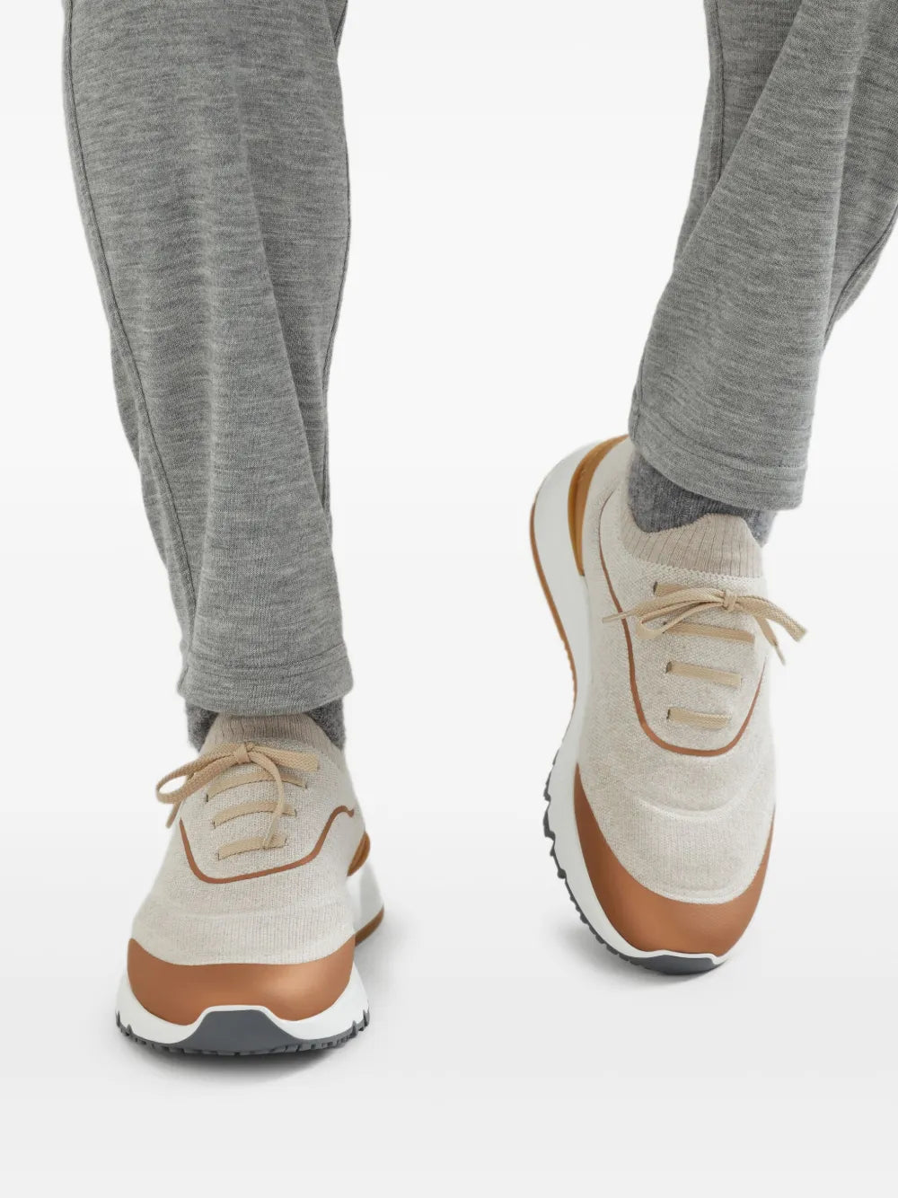 Beige knitted sneakers on model, lace-up with orange trim and grippy rubber sole
