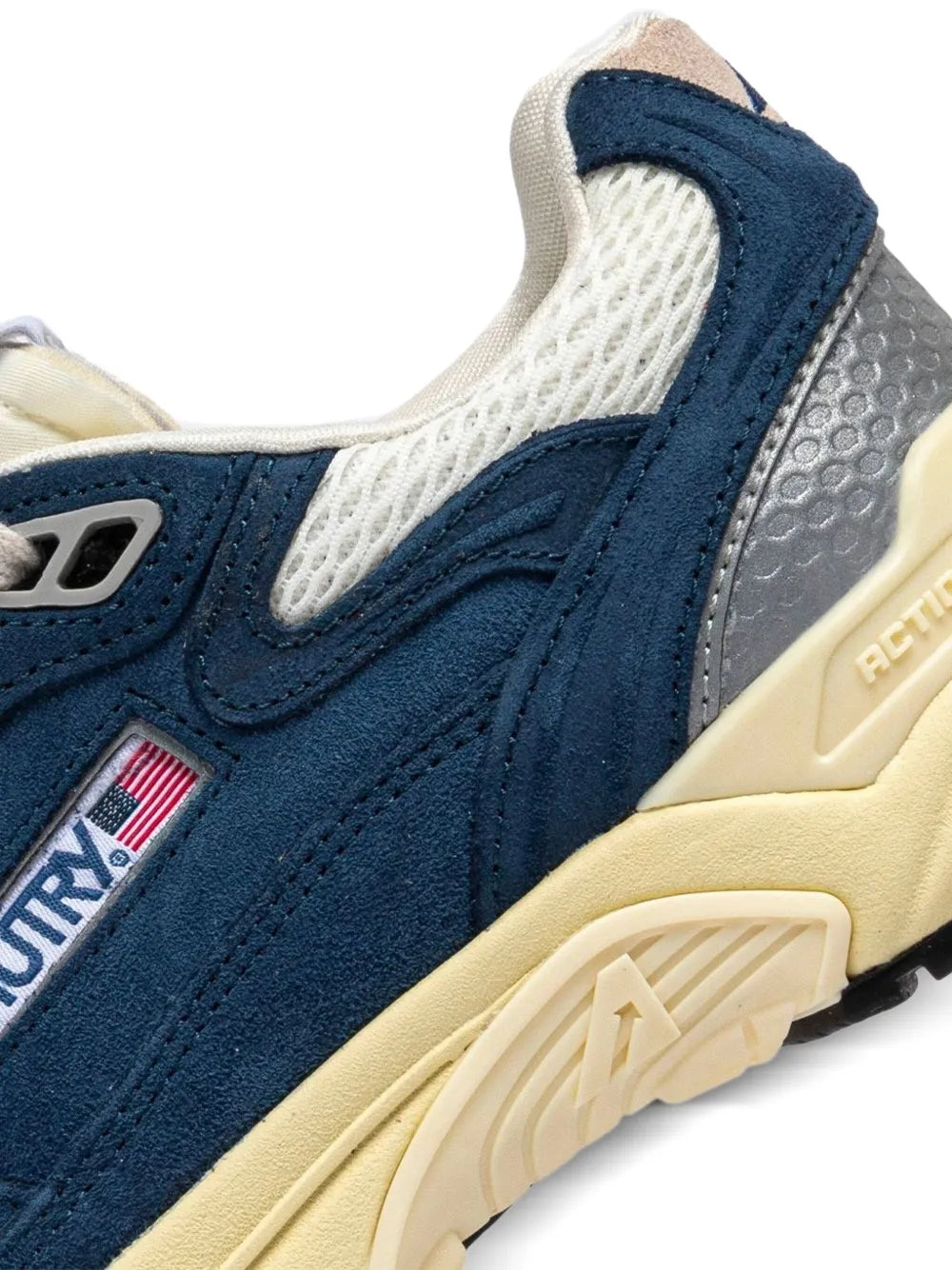 Navy suede sneaker detail with logo patch, cream mesh panel, and beige heel