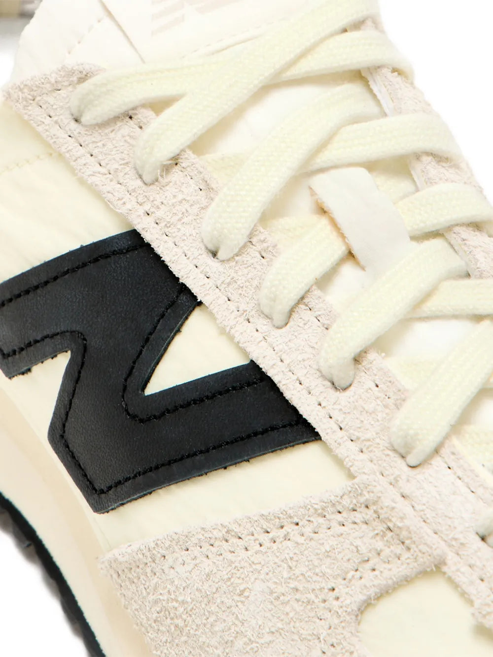 New Balance 471 cream sneaker close-up, lace-up with black N logo on textured upper