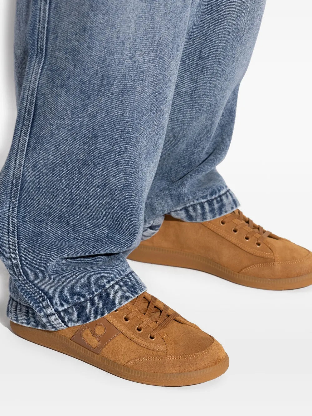 Brown suede lace-up sneaker worn with blue jeans, low-profile sole