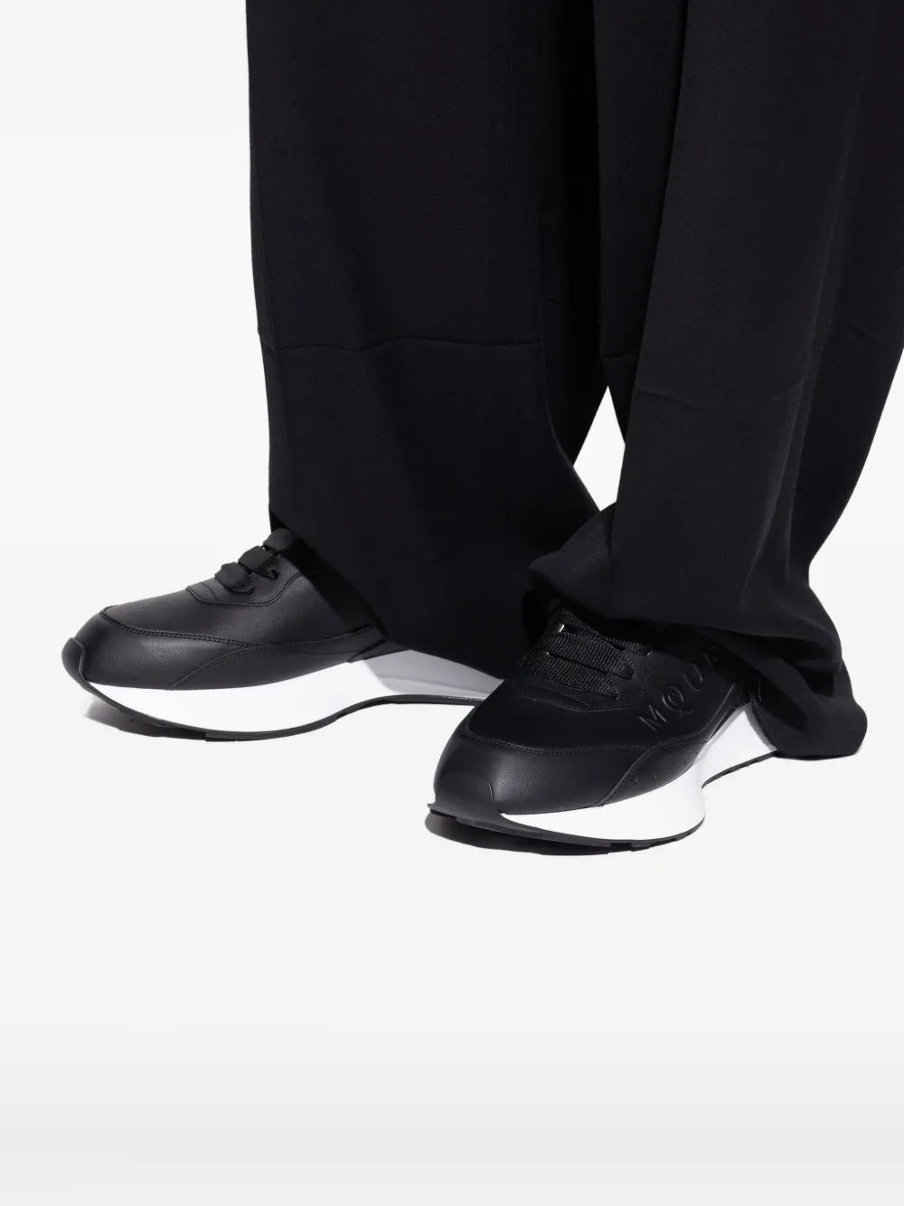 Black leather logo trainers worn with black trousers, white midsoles visible