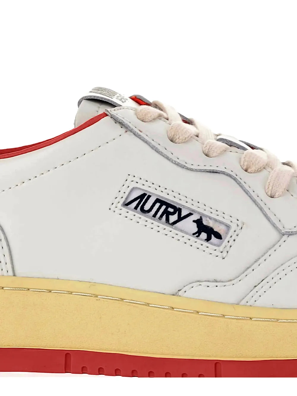 White Autry leather sneaker close-up with lace panel, logo patch, tan rubber sole