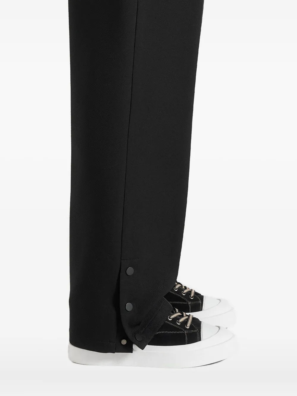Black suede sneakers with white sole, worn with long dark trousers