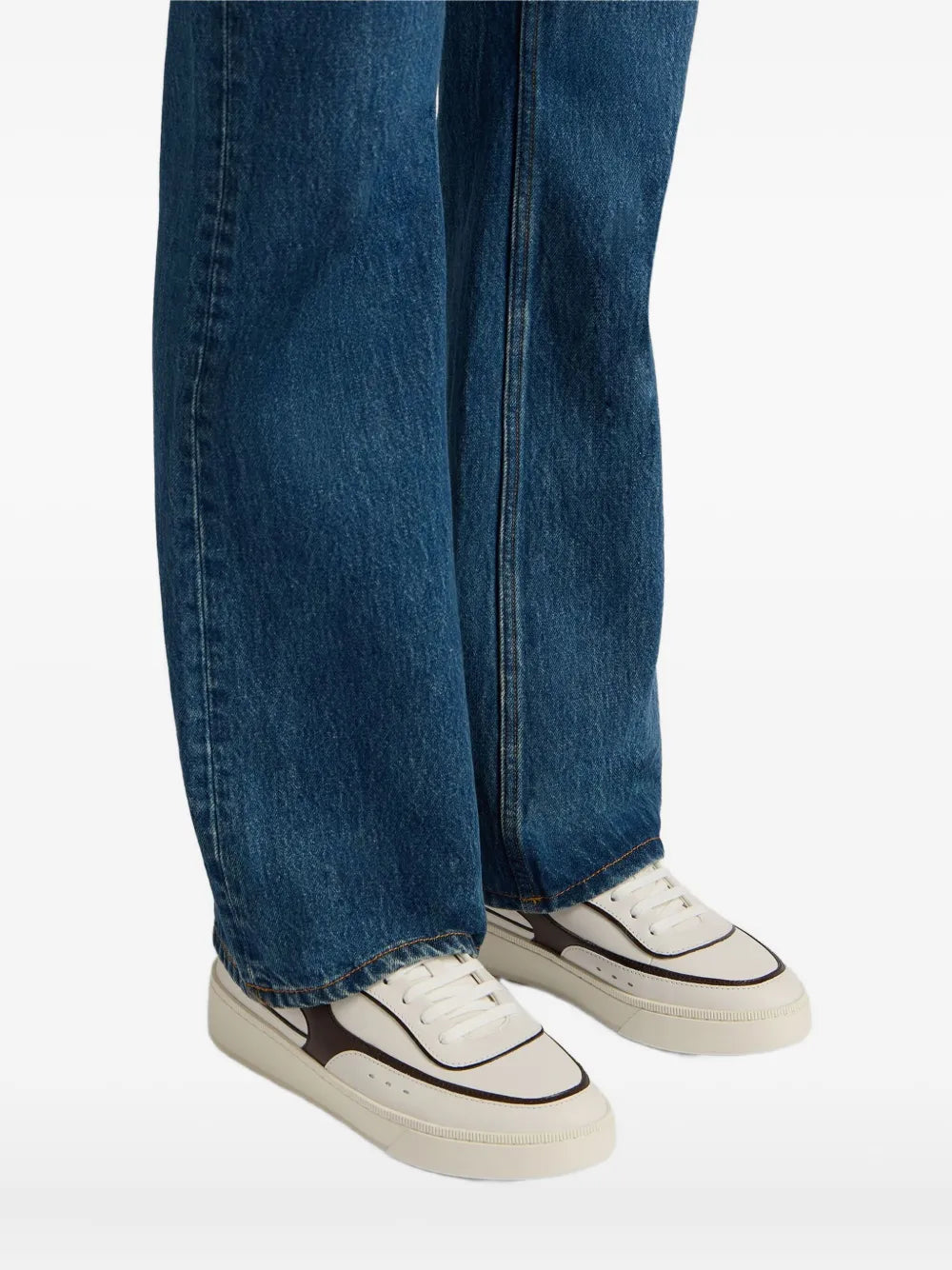White leather sneakers with dark brown trim worn with blue jeans