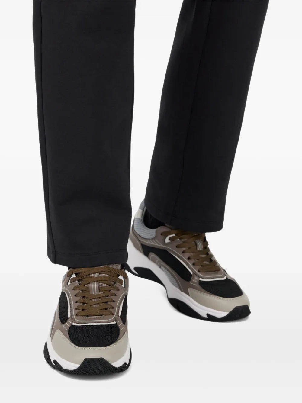 Brown-and-grey lace-up sneakers with white sole worn with black trousers