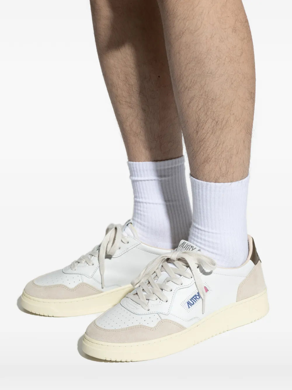White low-top sneakers with beige sole and panels, worn with white crew socks.
