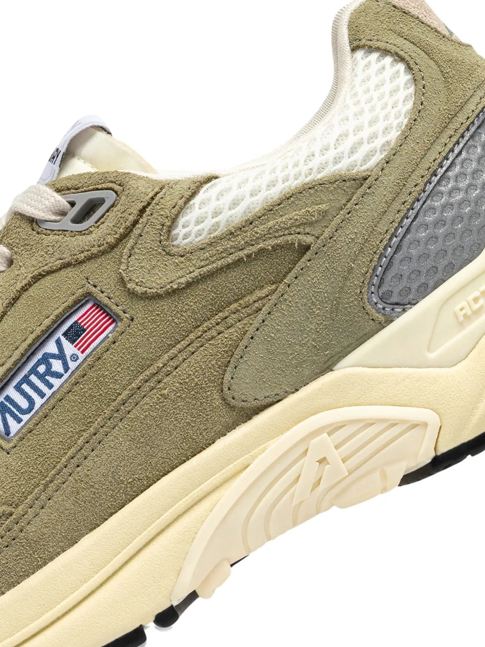 Olive green suede sneaker close-up with lace panel, logo patch, and rubber tread