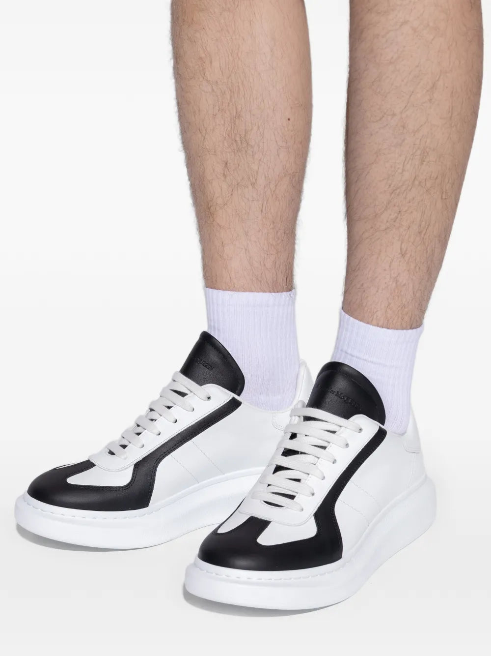 Alexander McQueen contrast-panel sneakers close-up, white leather with black panels and thick sole.