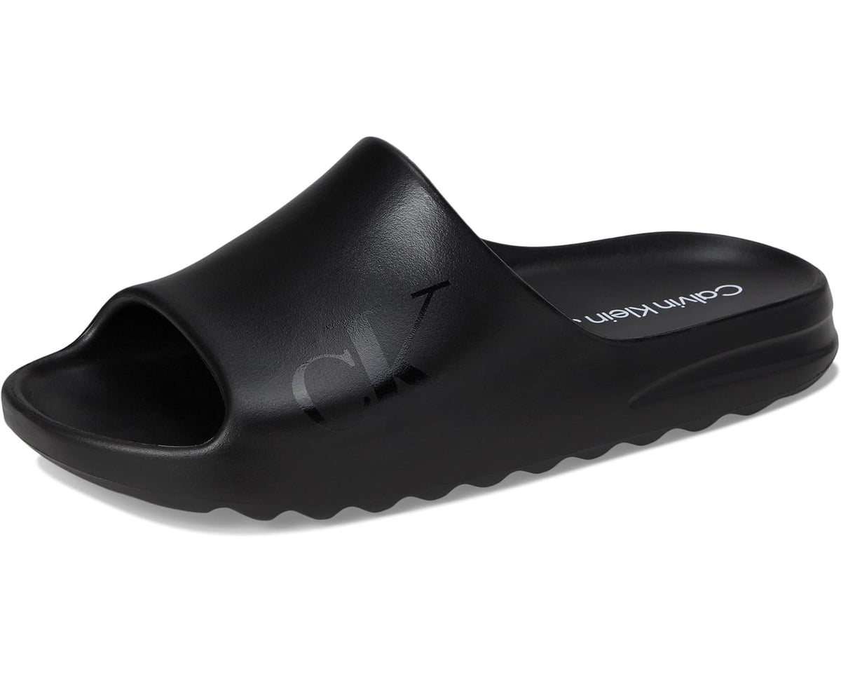 Black slide sandals with open toe, CK logo strap, and thick wave sole