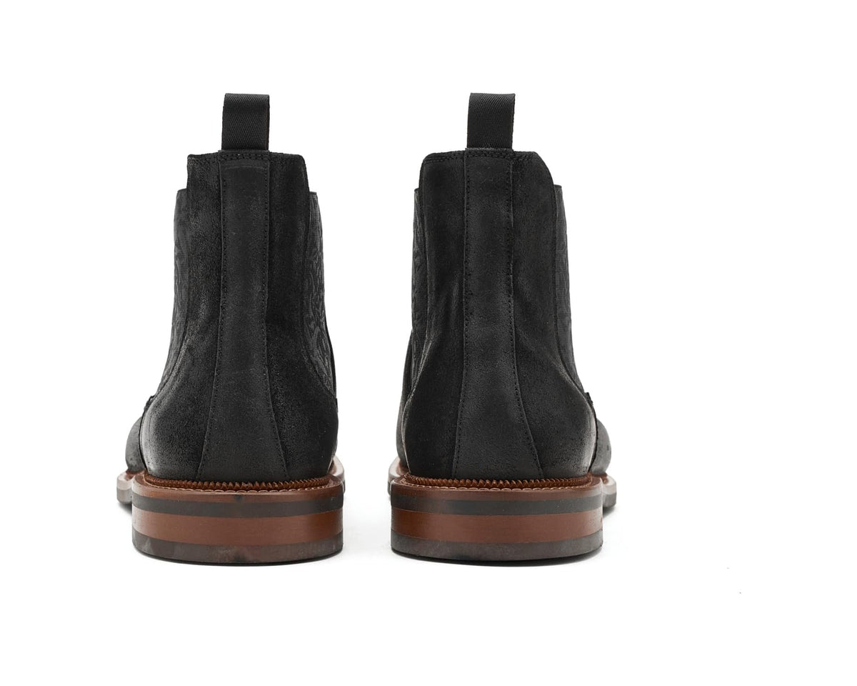 Back view of black suede Chelsea boots with pull tabs and brown welt outsole