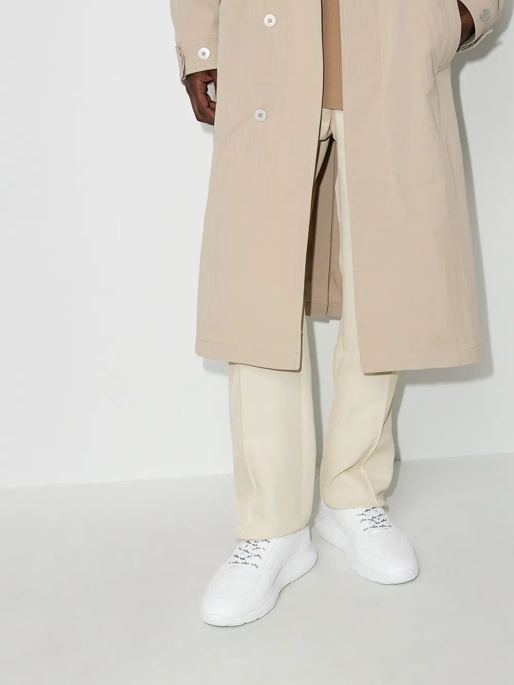 White low-top Hogan lace-up sneakers on feet with light pants.