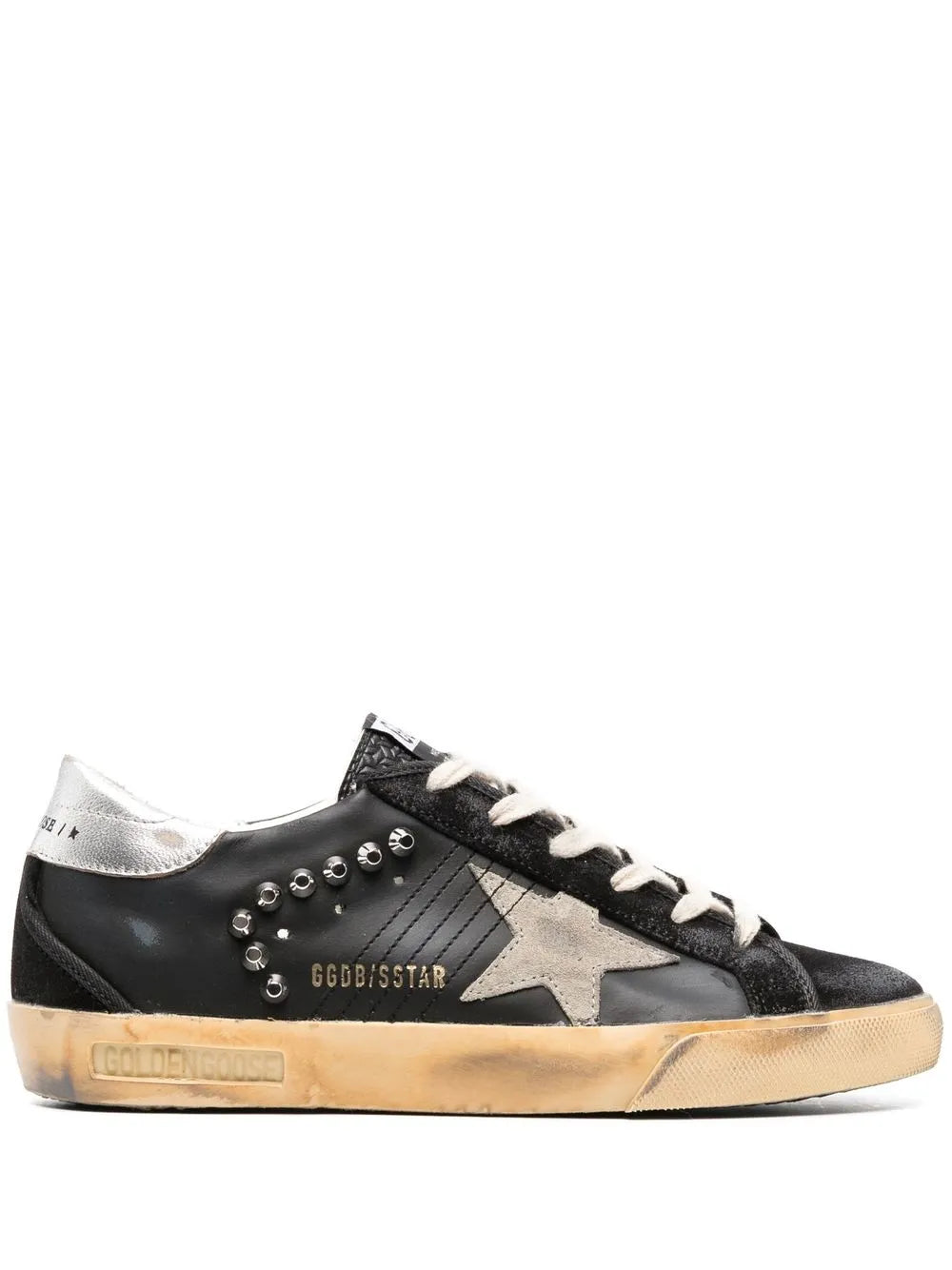 Black low-top sneakers with star patch, stud accents, white laces, tan sole.