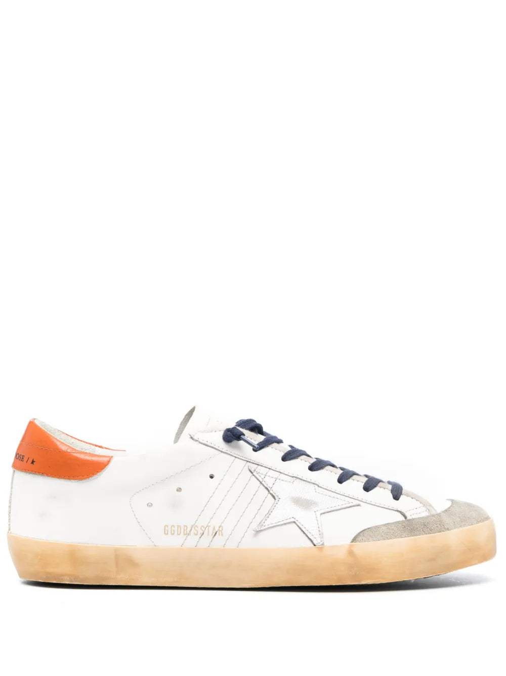 Off-white low-top sneakers with navy laces, star patch, tan sole and orange heel.