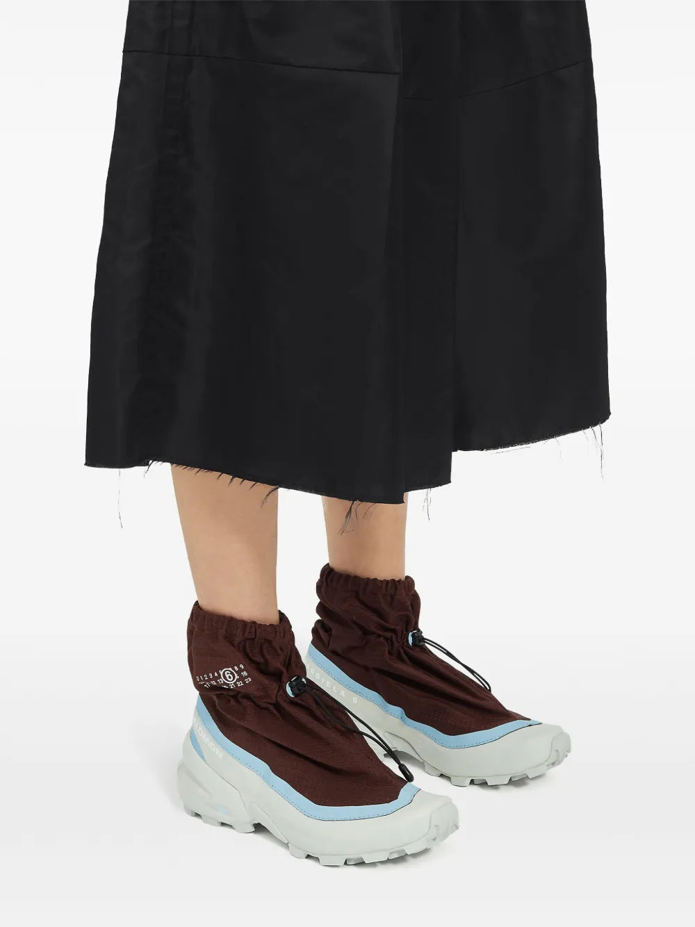 Brown mid-top sneakers with light blue trim and white lug sole worn with a black skirt