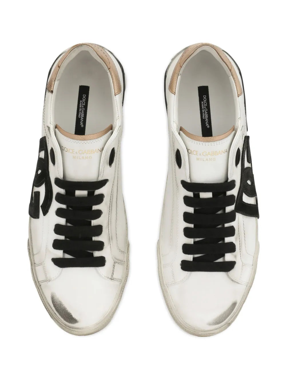 White low-top sneakers with black lace-up details and tan-lined tongue