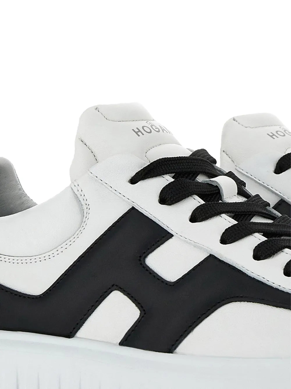 Close-up of white sneakers with black H-stripe panel and black lace-up eyelets
