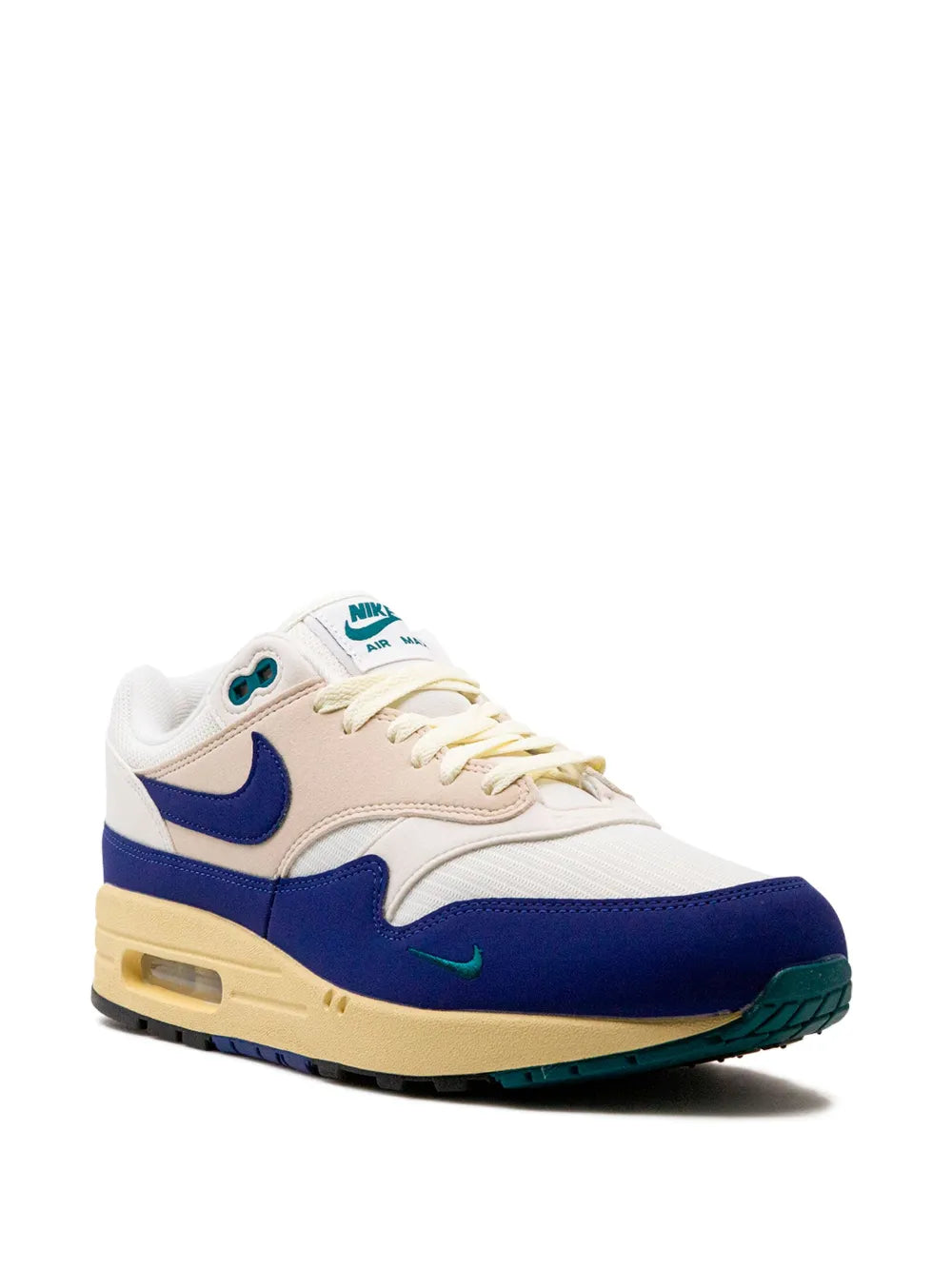 Nike Air Max 1 sneaker with white uppers, navy swoosh, beige sole, and teal trim