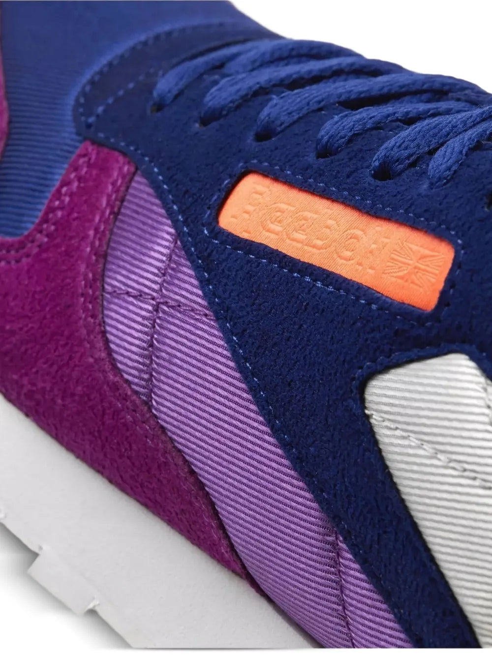 Reebok classic sneaker close-up of navy suede upper with orange tongue label