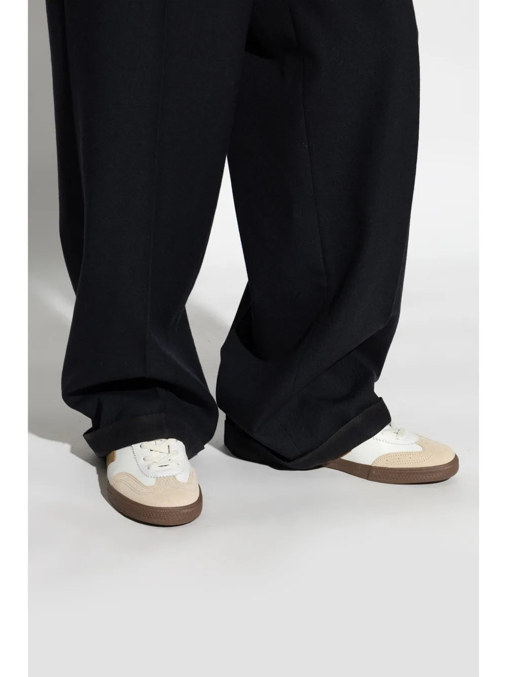 White low-top sneakers with brown outsole, worn with dark trousers