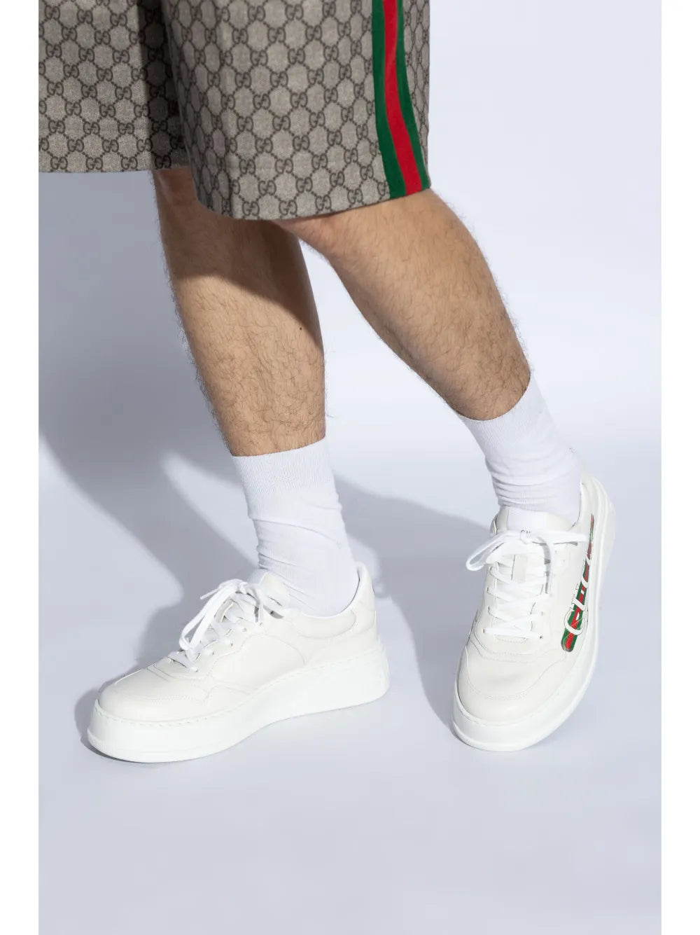 White Gucci logo-print sneakers on model with crew socks; shorts partially visible