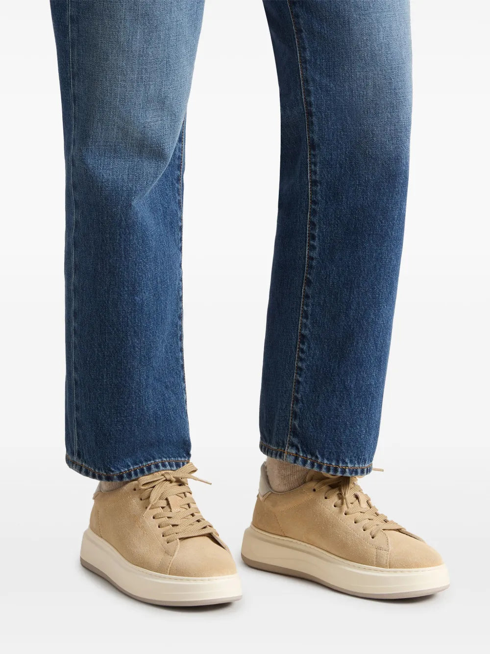 Beige suede sneakers on feet with denim jeans, lace-up style