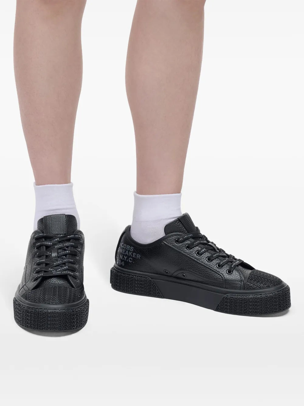 Black leather lace-up sneakers on feet with white socks, side view