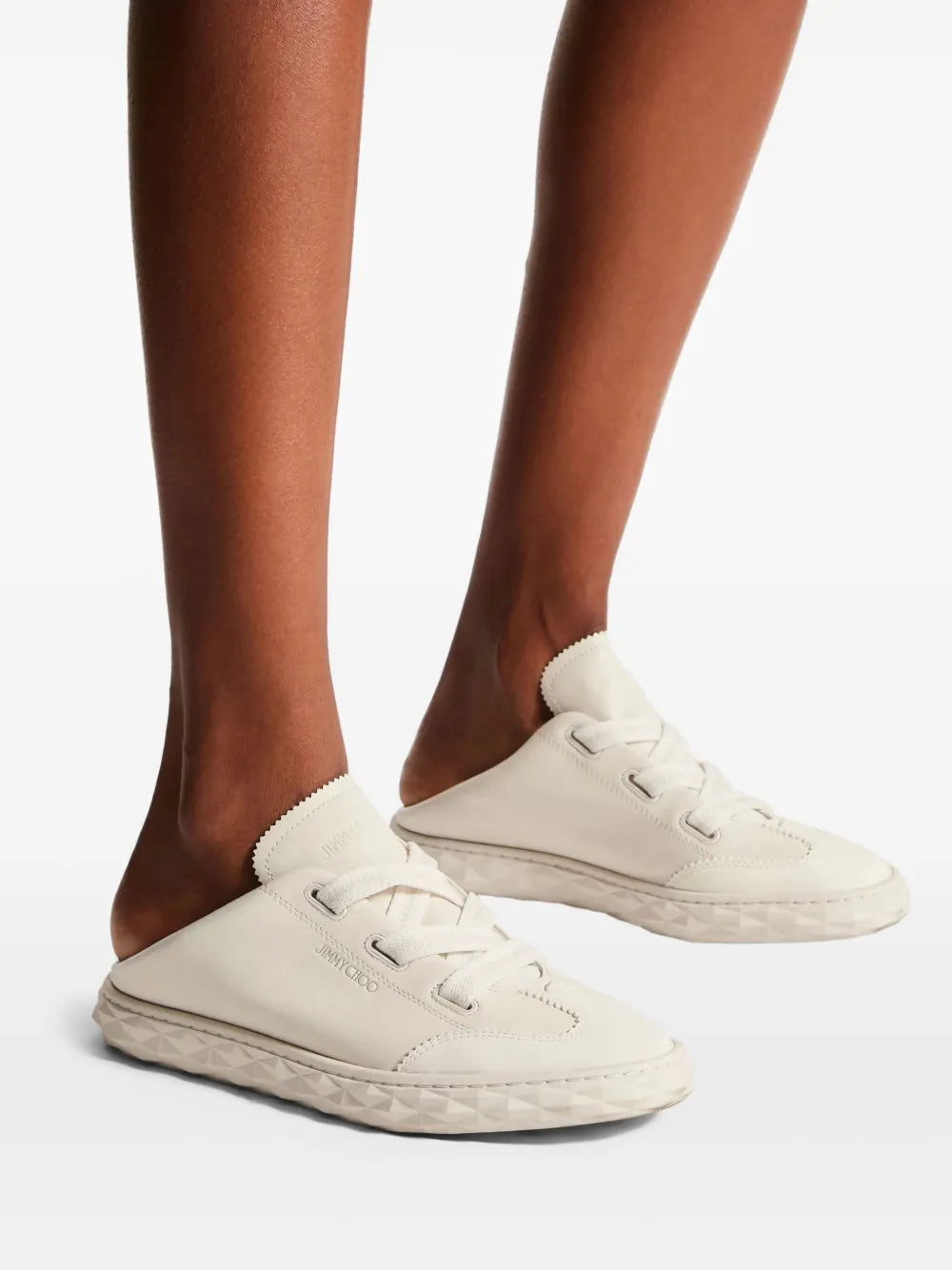 White low-top lace-up sneakers worn with jeans, rubber sole and logo accents