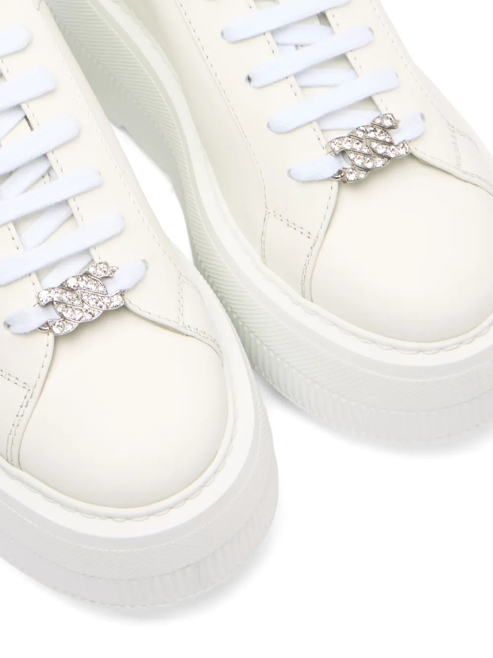 Close-up of white leather sneakers with silver jeweled strap detail on the vamp