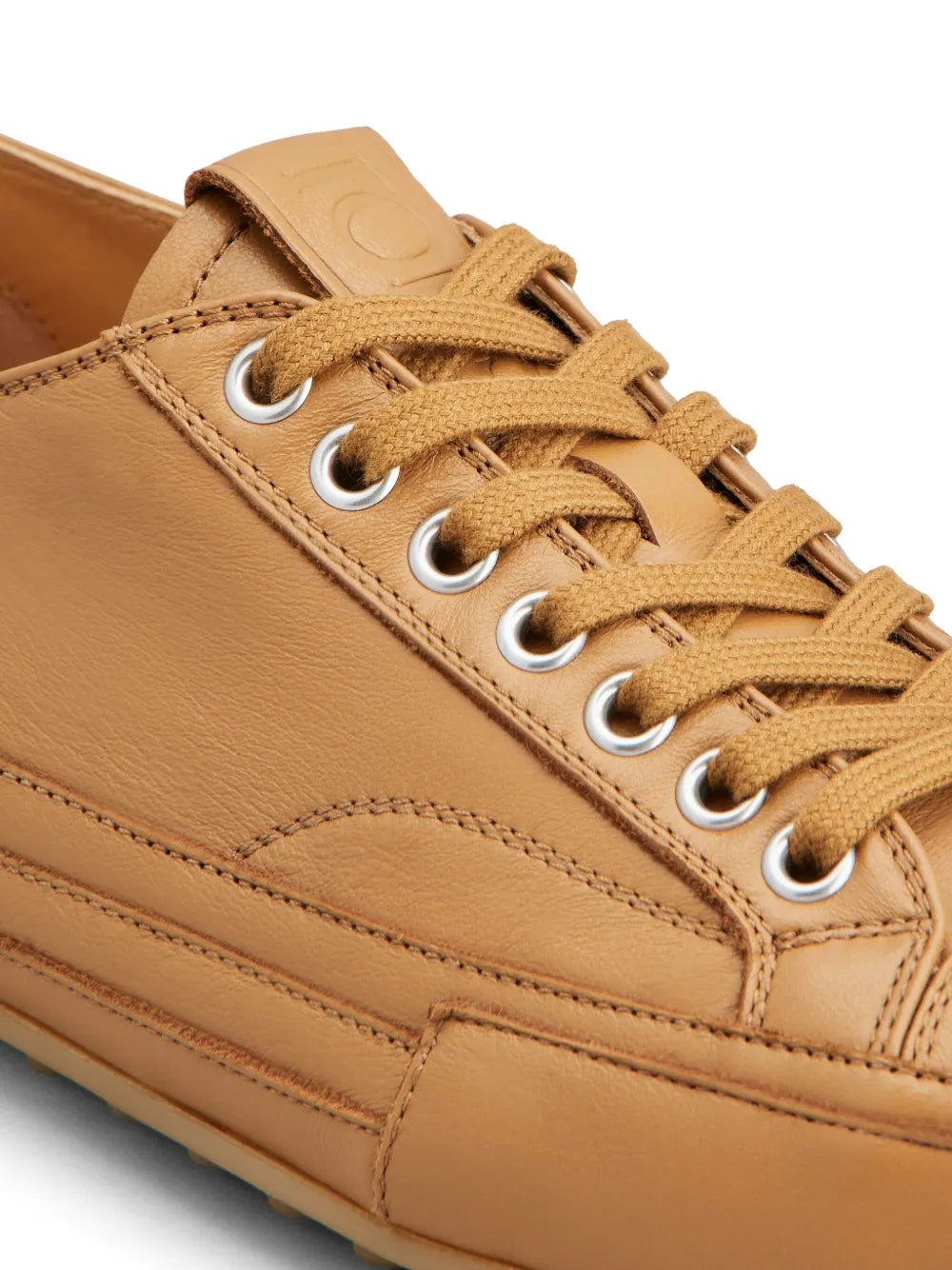 Tan leather sneaker upper close-up with lace eyelets and stitching