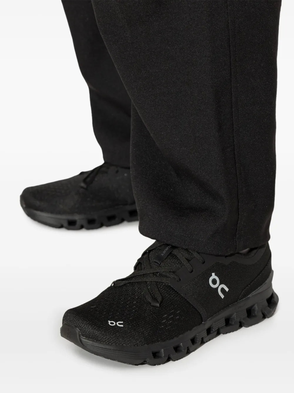 Black lace-up running shoe close-up on black pants, On logo and pod outsole